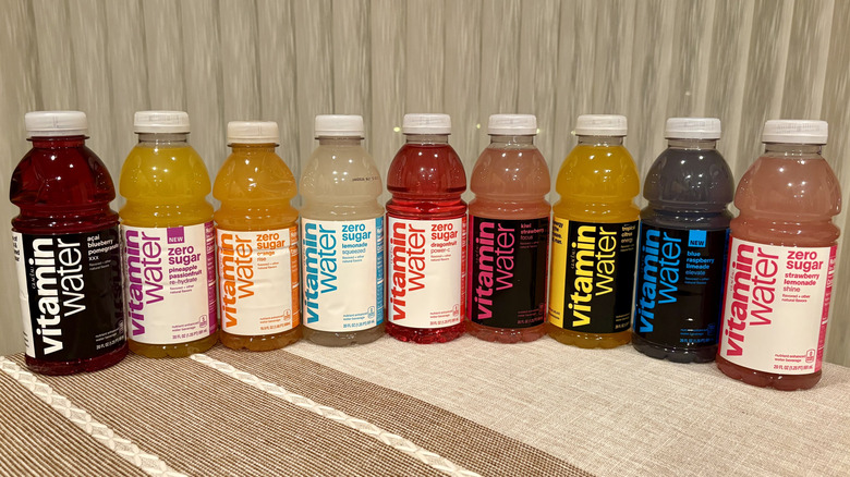 Nine Vitaminwaters lined up in front of a white curtain