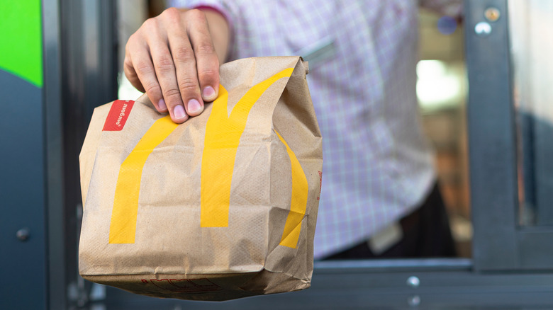 A person handing a bag of McDonald's food to a customer at a drive-thru