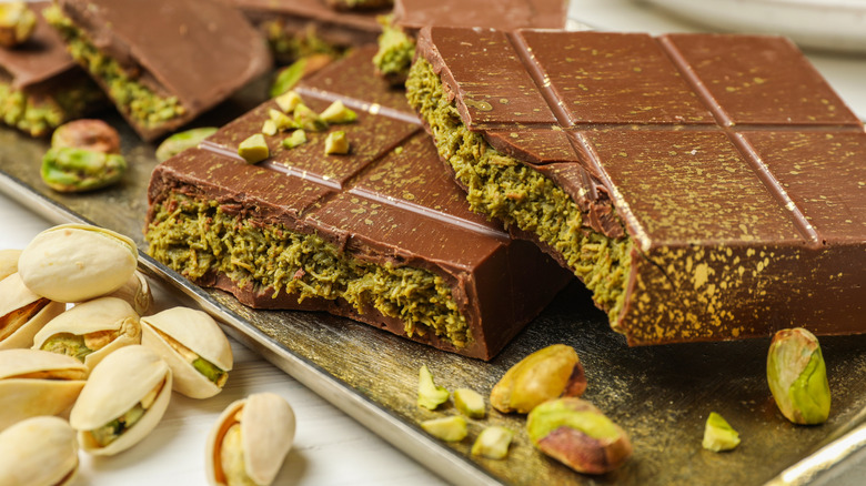 pieces of a dubai chocolate bar on a sheet pan surrounded by pistachios in the shell