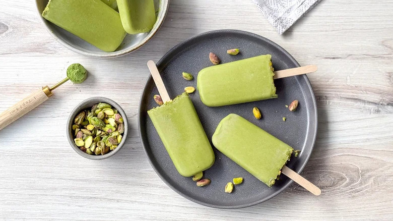 pistachio popsicles on a black plate surrounded by pistachio nuts