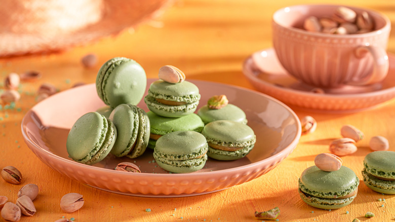 pistachio macrons on a peach background on a peach plate surrounded by pistachios