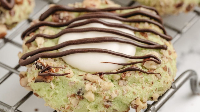 a close up picture of a pistachio thumbprint cookie drizzled with chocolate on a cooling rack