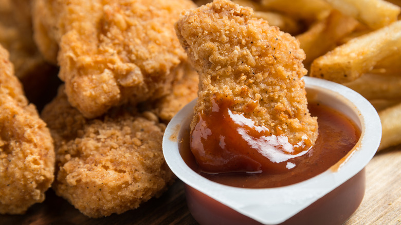 A fast food chicken nugget in a container of dipping sauce