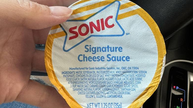 A person holding a container of Sonic Signature Cheese Sauce