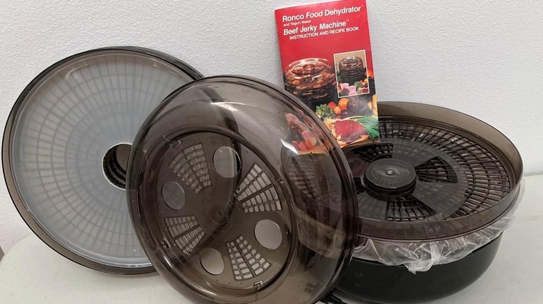 Disassembled 1990s Ronco food dehydrator with instruction book on a table