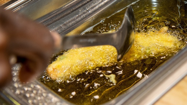 A woman uses a spoon to gently maneuver battered fish in a deep-fryer.
