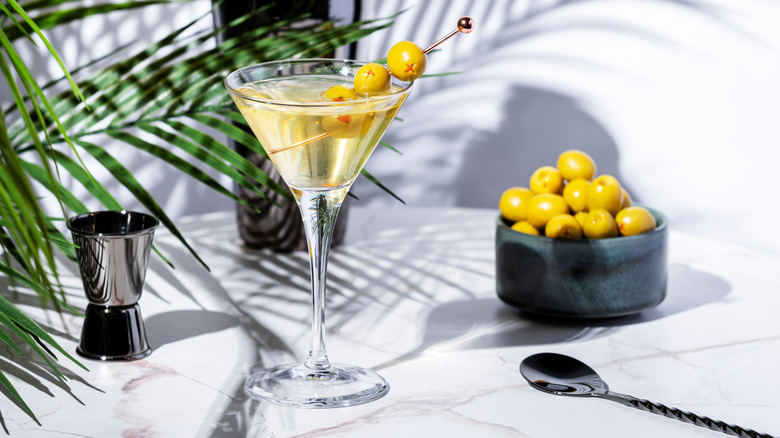 dirty martini in a glass with olives nearby