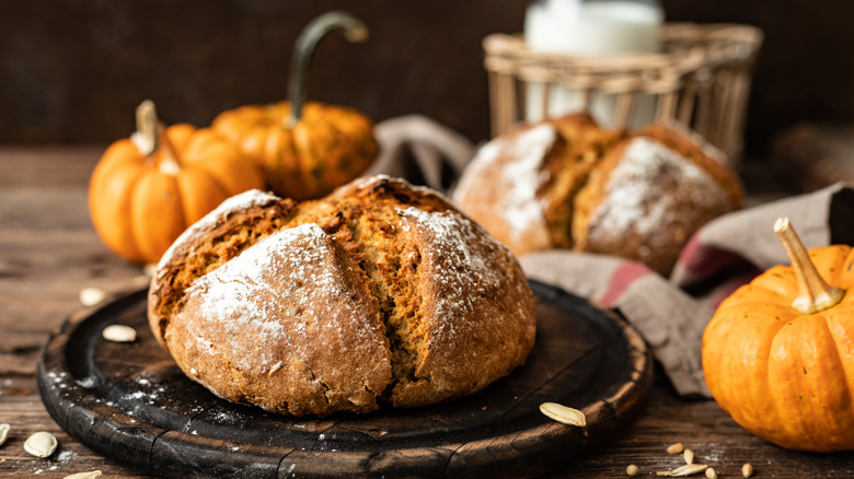 Pumpkin loaf on wooden cutting board with decorative pumpkins in background.
