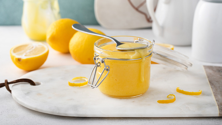 A jar of lemon curd arranged with whole and half lemons.