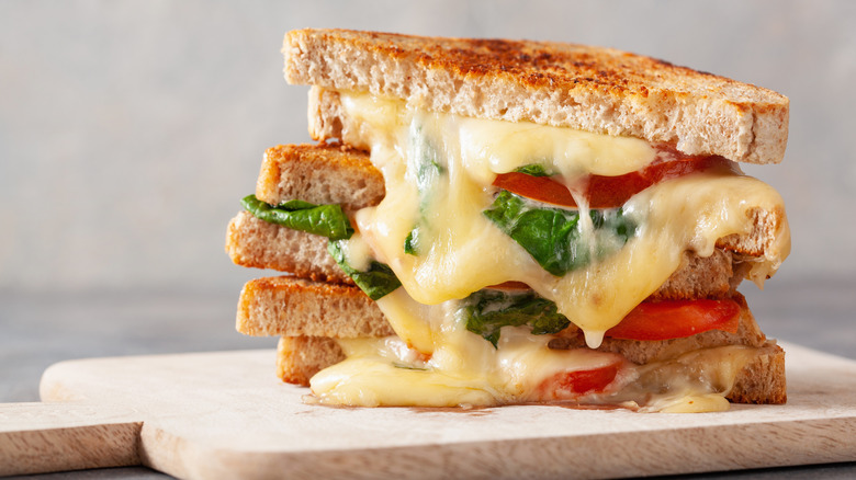 A grilled cheese with tomato and basil on a wooden cutting board.
