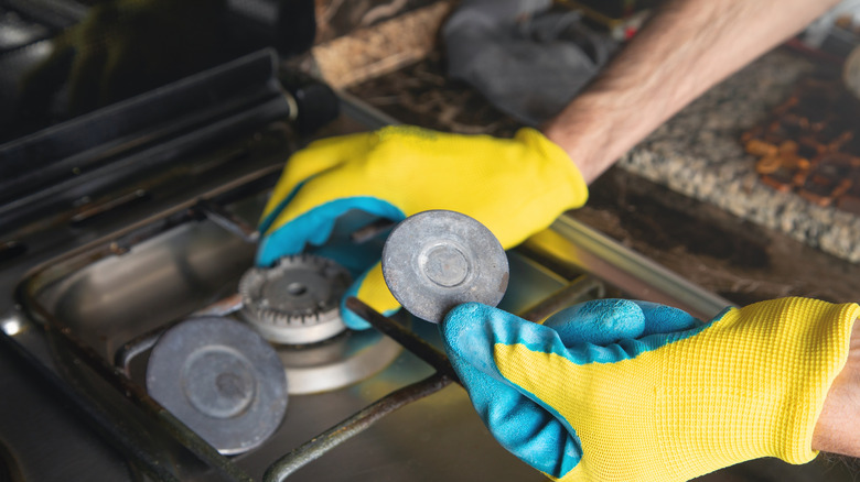Person with yellow and blue gloves repairing gas stove