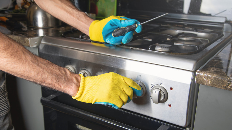 Person with blue and yellow gloves repairing gas stove