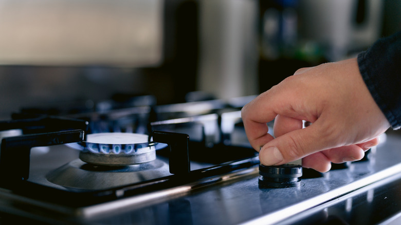 A hand turns on a stove fired by natural gas