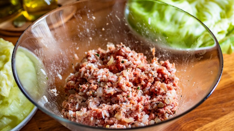 Ground beef in a glass bowl next to cabbage leaves.