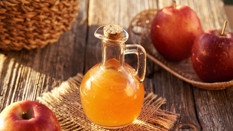 Glass jug of apple cider with apples on the side