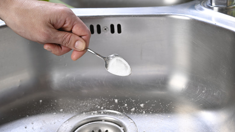 hand sprinkling a spoonful of baking soda into a stainless steel sink