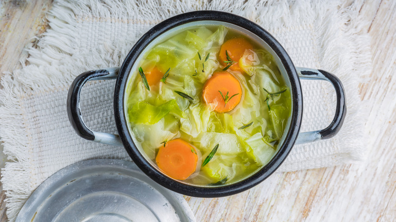 Cabbage soup in pot with sliced carrots, over a napkin