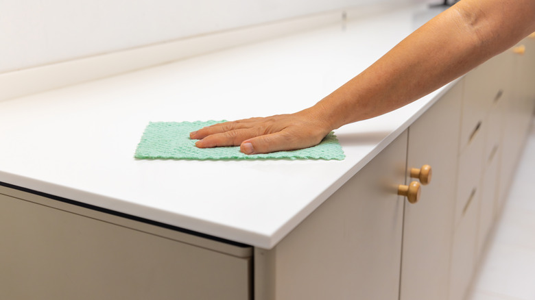 A hand wiping down a clean acrylic countertop with a soft cloth
