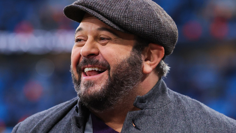 A smiling Adam Richman looking to the side, wearing a newspaper boy hat