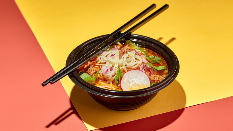 Bowl of birria ramen on bright background with chopsticks