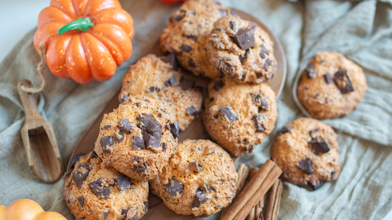 A small pumpkin figurine beside a plate of chocolate chip cookies.