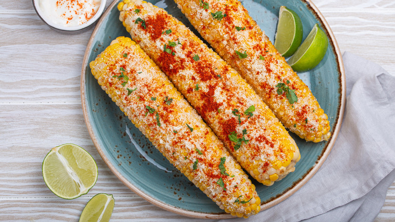 Elotes Mexican street corn cob covered in spices and cheese being served on plate