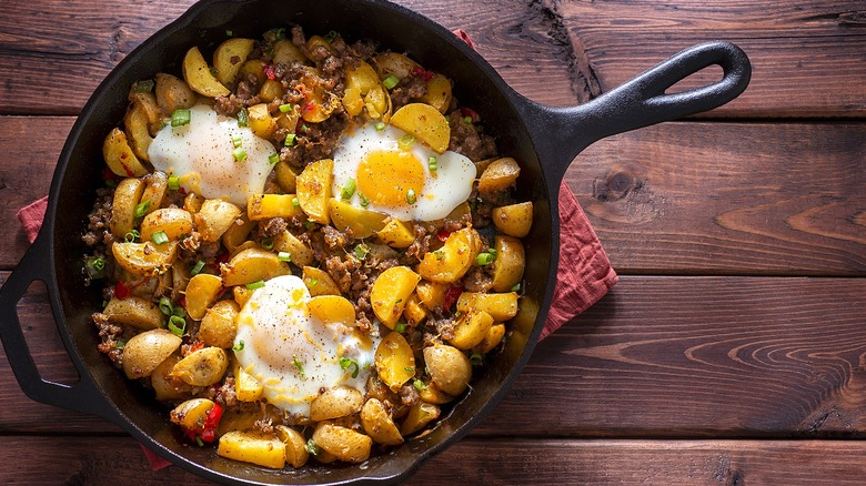 Spiced breakfast potatoes with crumbled sausage and fried eggs in a cast-iron skillet