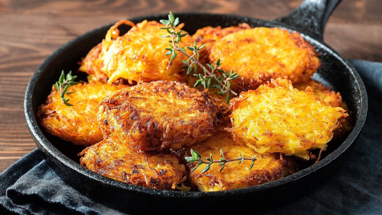 Cooked, round hash brown patties in a cast-iron pan topped with fresh herbs