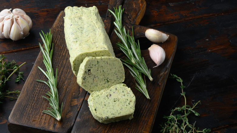 A log of herb compound butter on a wooden cutting board.