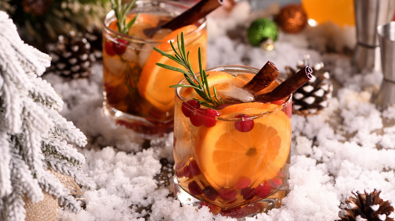 two whiskey cocktails with orange slices, herb sprigs, and cinnamon stick