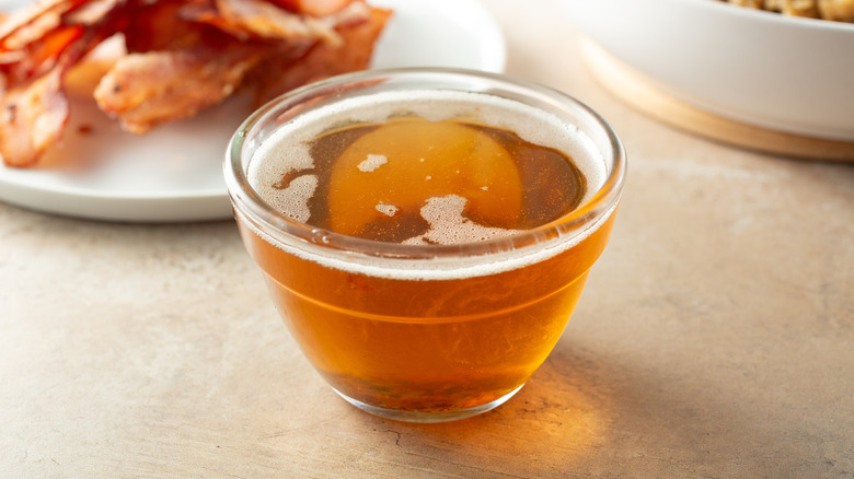 A clear glass bowl of rendered bacon fat.