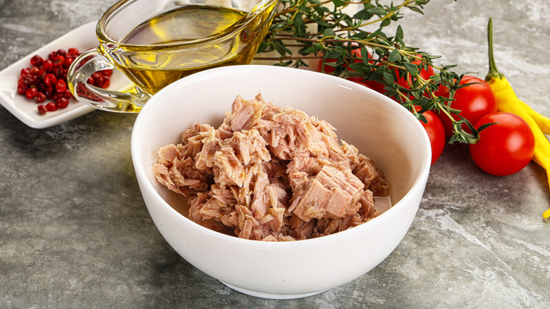 A bowl of canned tuna next to oil and tomatoes.