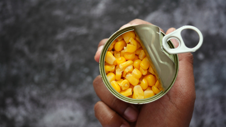 Person holding open canned sweet corn close up