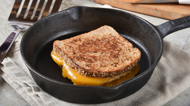 A melty grilled cheese sandwich on grain bread in a cast iron pan.