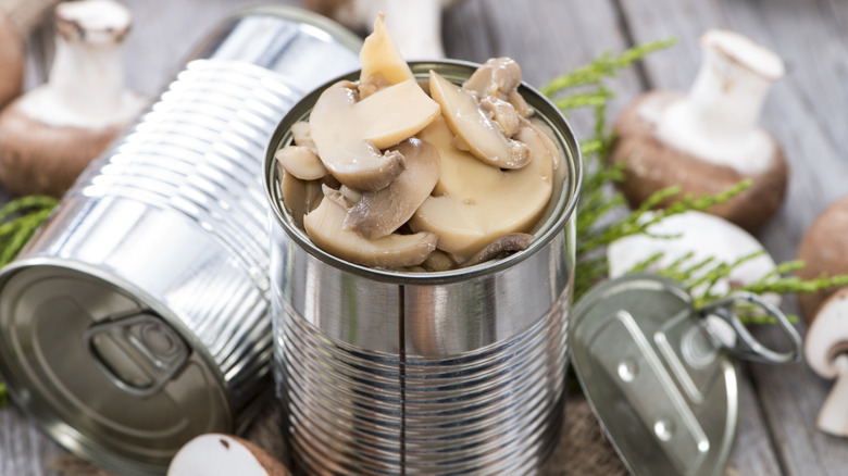 White button mushrooms in a can on a wooden table.