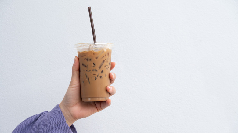 Hand holding iced coffee against white wall