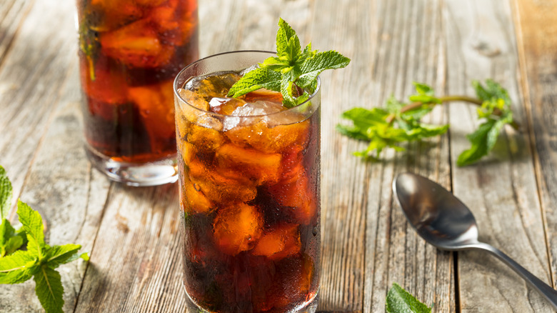 Two glasses of fresh mint iced coffee on wood table next to spoon.