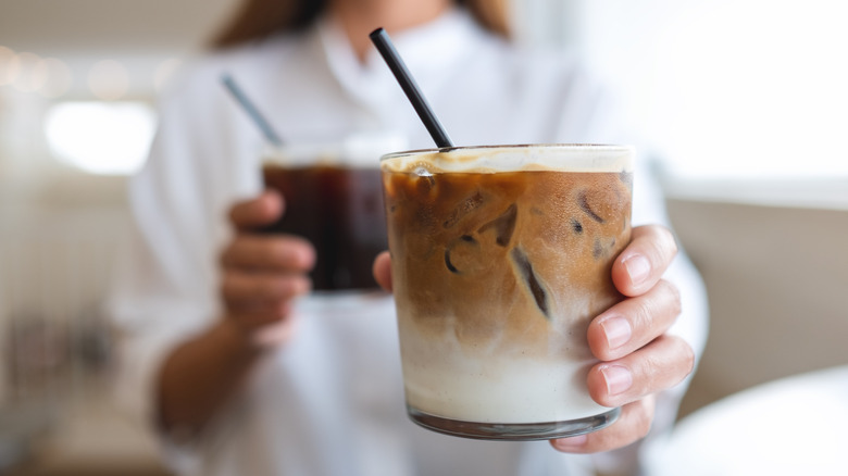 Closeup of person holding glass of iced coffee with milk.