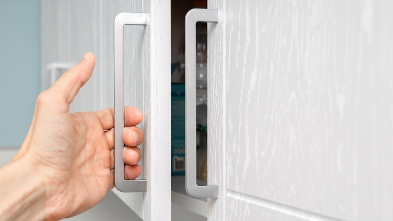 Hand pulling on a silver kitchen cabinet handle.