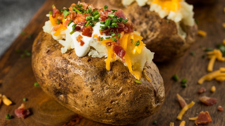 loaded baked potatoes on wooden cutting board