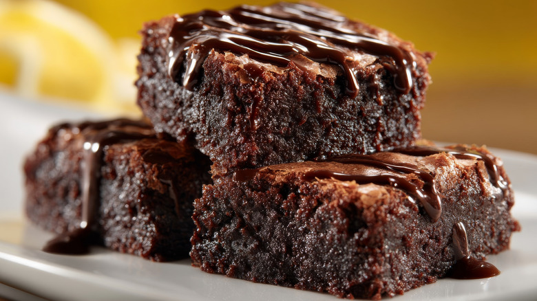 Delicious chocolate brownies drizzled with rich chocolate sauce, stacked on a white plate