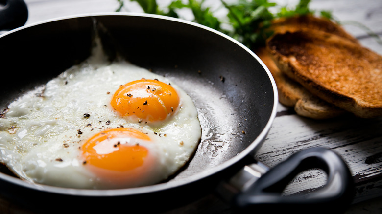 two fried eggs seasoned with salt and pepper in a pan