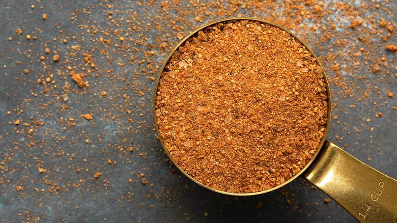 Old Bay Seasoning in a gold 1/4 cup measuring cup on a gray surface.