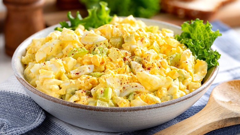 Egg salad in a shallow bowl with a few pieces of green lettuce.