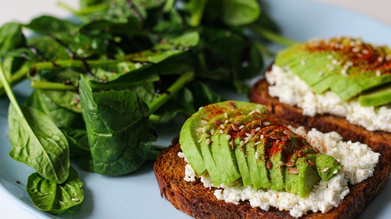 Rye toast with avocado and seeds and chili seasoning as toppings and a side of salad
