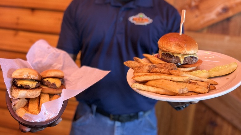 Texas Roadhouse waiter holding a basket of sliders and fries, and a plate of fries and a cheeseburger