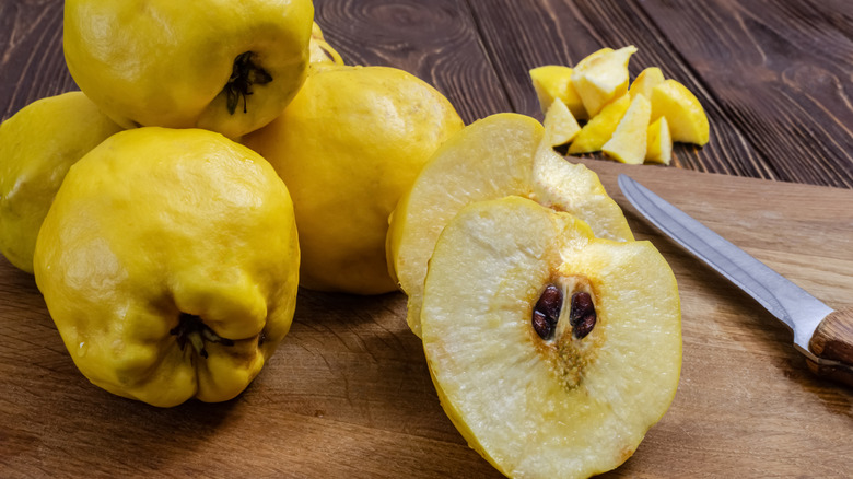 Quince fruits, some whole and one sliced in half, on a wooden cutting board.