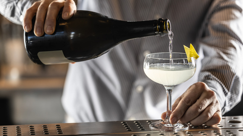 bartender pouring sparkling wine into a French 75 cocktail