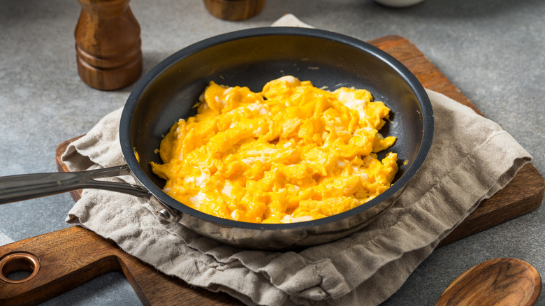 A pan of scrambled eggs on top of a cutting board.