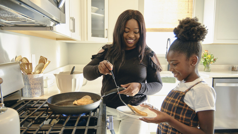 A mom serves a freshly cooked pancake from the pan to her daughter's plate